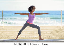 Black woman, afro hairstyle, doing yoga in warrior asana in the beach Black woman, afro hairstyle, doing yoga in warrior asana in the beach