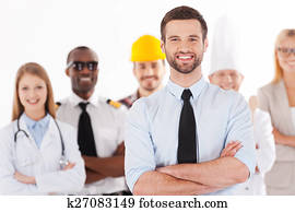 wenn, ich, wachsen, herauf, ich, wille, sein, a, businessman., sicher, junger mann, in, hemd band, beibehaltung, verschränkte arme, und, lächeln, während, menschengruppe, in, verschieden, berufe, stehen, in, dass, hintergrund