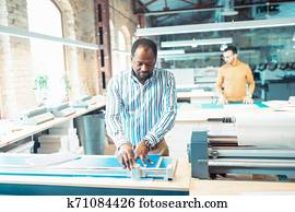 Dark-skinned bearded graphic designer making measurements for paper Dark-skinned bearded graphic designer making measurements for paper