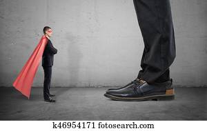 A tiny businessman in a superhero cape stands facing giant man with only his feet seen.