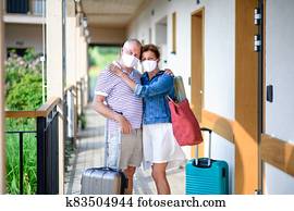 Senior couple with face masks and luggage outside apartment on holiday. Senior couple with face masks and luggage outside apartment on holiday.