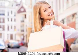 Nice day for shopping. Rear view of beautiful young cheerful woman holding shopping bags and looking over shoulder while standing outdoors