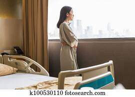 Depressed asian woman patient standing is hospital ward look out window.