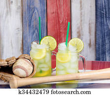 Glass jars filled with cold lemonade along with baseball sporting objects on USA national colors for the holiday season 