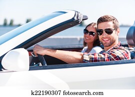 Traveling with comfort. Happy young couple enjoying road trip in their white convertible while both looking at camera and smiling