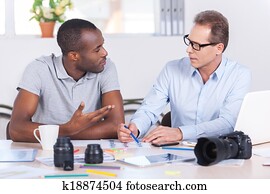 Working on creative project together. Two confident business people in casual wear sitting together at the table and discussing something