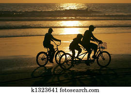 Family riding bikes along the beach at sunset.