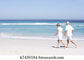 Senior Couple On Holiday Running Along Sandy Beach