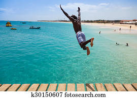 Teenage Cape verdean boy jumping on the turquoise  water of Santa Maria beach in Sal Cape Verde - Cabo Verde