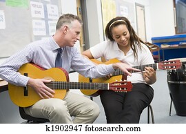 Schoolgirl and teacher playing guitar in music class