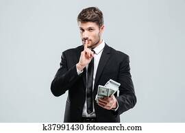 Handsome young businessman holding money and showing silence sign Handsome young businessman holding money and showing silence sign