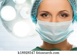 Young woman doctor in cap and face mask in surgery room interior Young woman doctor in cap and face mask in surgery room interior
