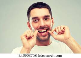 man with dental floss cleaning teeth over gray man with dental floss cleaning teeth over gray