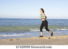 Young Woman In Fitness Clothing Running Along Beach