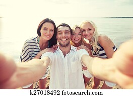 happy friends on beach and taking selfie