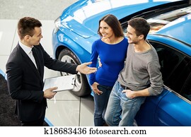 Buying their first car together. High angle view of young car salesman standing at the dealership telling about the features of the car to the customers