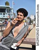 Young male tourist eating pizza at the beach