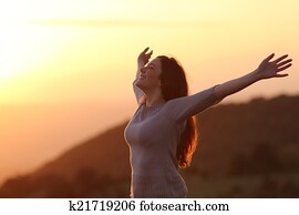 Woman at sunset breathing fresh air raising arms