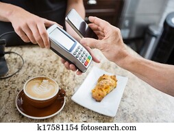 Cropped image of customer paying through mobilephone over electronic reader at cafe counter Cropped image of customer paying through mobilephone over electronic reader at cafe counter