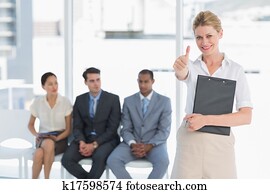 retrato, de, un, mujer joven, el gesticular, pulgares arriba, con, gente, esperar, para, entrevista de trabajo, en, un, brillante, oficina