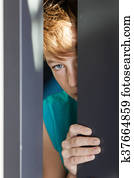 Serious teen peeking from between door and wall