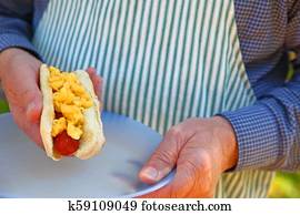 Backyard cook holding macaroni and cheese hot dog Backyard cook holding macaroni and cheese hot dog