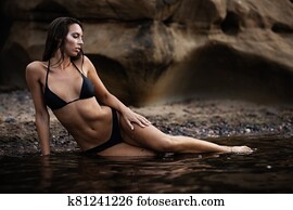 Summertime recreation and travel concept. Beautiful tanned young fashion model in bikini posing on the sea coast. Woman in swimsuit with wet hair and body lying on a beach. Summertime recreation and travel concept. Beautiful tanned young fashion model in bikini posing on the sea coast. Woman in swimsuit with wet hair and body lying on a beach.