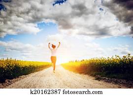 Happy young woman running and jumping for joy towards sun Happy young woman running and jumping for joy towards sun