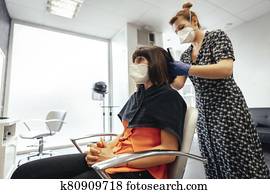 Hairdresser with security measures for the covid-19, new normality, social distance. Cutting the ends of a brunette client with a mask