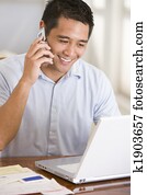 Man in dining room on cellular phone using laptop smiling