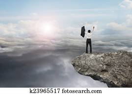 businessman cheering on cliff with natural sky daylight cloudsca