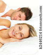 Couple lying in bed and woman smiling at the camera