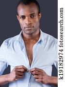 Wearing his favorite shirt. Handsome young black man dressing up his shirt and smiling at camera while standing against grey background