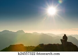 lonely sad person sits on summit of mountain at sunset 