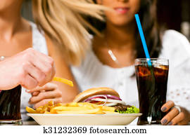 Two women eating hamburger and drinking soda