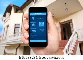 male hand hold a phone with system smart house on a screen on the background of the house