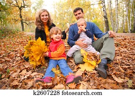 Family of four with yellow maple leaves sits in wood in autumn