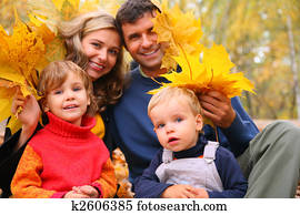Family of four with yellow maple leaves in wood in autumn