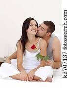 Lovers sitting on bed with a rose