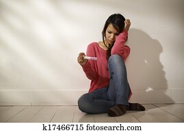 Sad Asian girl looking at pregnancy test sitting on floor