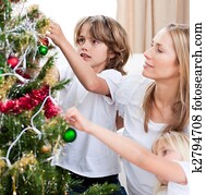 Children hanging Christmas decorations with their mother