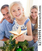 Father lifting his daughter to put the Christmas star on top of the tree at home