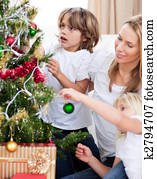 Smiling Mother and her children decorating a Christmas tree