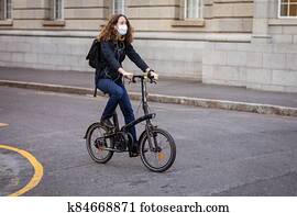 Caucasian woman wearing a protective mask and earphones, and biking in the streets Caucasian woman wearing a protective mask and earphones, and biking in the streets