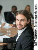 sonriente, joven, hombre de negocios, en, traje, mirar cámara del juez, en, reunión