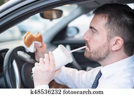 Man eating an hamburger and driving seated in car Man eating an hamburger and driving seated in car