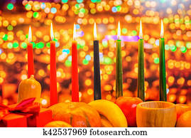 Kwanzaa celebration concept with seven candles red, black and green, gift box, pumpkin, bowl and fruit on light blur bokeh background, close up Kwanzaa celebration concept with seven candles red, black and green, gift box, pumpkin, bowl and fruit on light blur bokeh background, close up