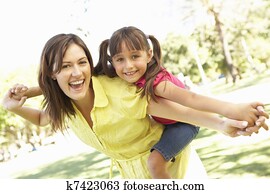 Mother Giving Daughter Ride On Back In Park Mother Giving Daughter Ride On Back In Park