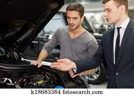 Power engine. Handsome young salesman showing all the car features to the customer