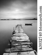 Looking over a desolate pier and a boat, black and white